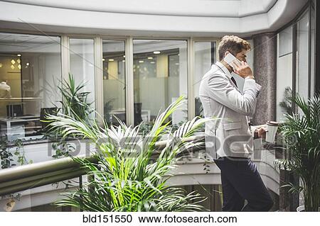 Stock Image - Caucasian businessman talking on cell phone on office balcony. Fotosearch