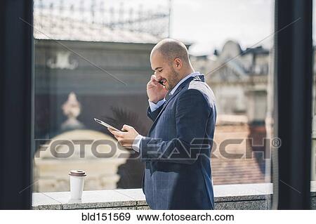 Stock Photo - Caucasian businessman talking on cell phone at window. Fotosearch