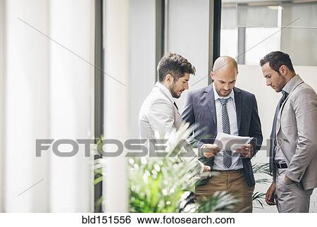 Stock Photograph - Caucasian businessmen reading paperwork in office corridor. Fotosearch