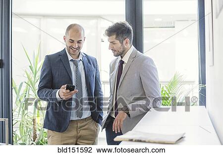 Caucasian businessmen using cell phone in office lobby View Large Photo Image Stock Image - Caucasian businessmen using cell phone in office lobby. Fotosearch