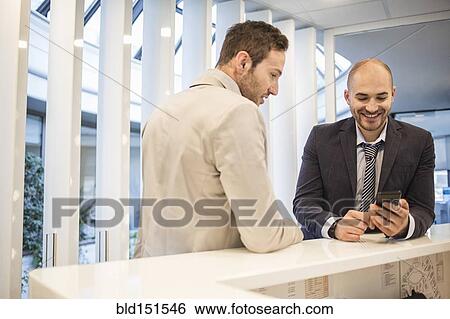 Stock Photograph - Caucasian businessmen using cell phone in office lobby. Fotosearch