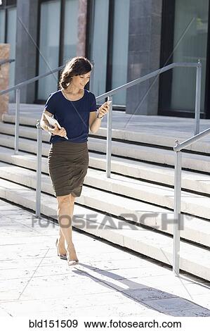 Stock Photo - Caucasian businesswoman carrying cell phone and digital tablet outdoors. Fotosearch