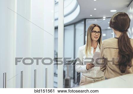 Stock Image - Caucasian businesswoman talking in office corridor. Fotosearch
