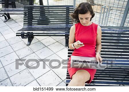 Caucasian businesswoman using laptop and cell phone on bench View Large Photo Image Stock Photo - Caucasian businesswoman using laptop and cell phone on bench. Fotosearch