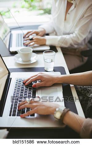 Stock Photograph - Caucasian businesswomen working at laptops at desk. Fotosearch