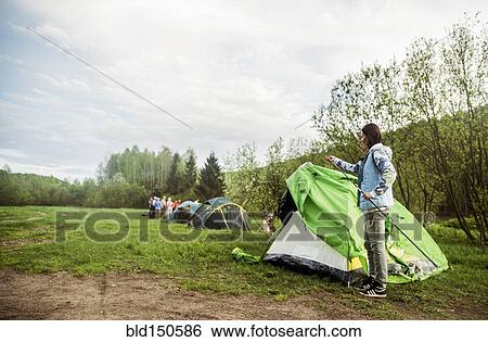 Stock Photograph - Caucasian camper assembling tent in remote field. Fotosearch