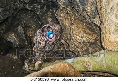 Stock Photograph - Caucasian climber exploring rock formation cave. Fotosearch
