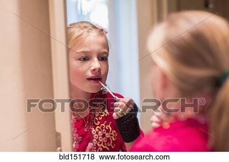 Stock Photo - Caucasian girl applying lip gloss in mirror. Fotosearch