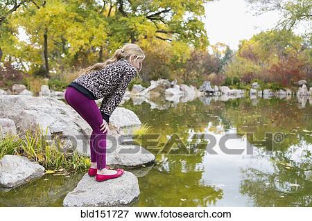 Stock Photo - Caucasian girl crouching on rock in pond. Fotosearch