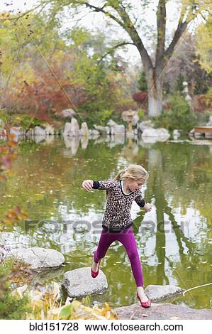 Stock Photo - Caucasian girl jumping on rocks in pond. Fotosearch