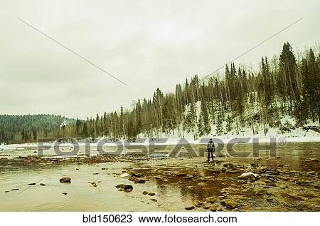 Stock Image - Caucasian hiker standing in rocky remote river. Fotosearch