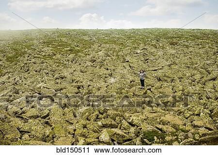 Stock Image - Caucasian hiker standing with arms outstretched in rocky field. Fotosearch