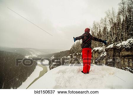 Stock Photo - Caucasian hiker standing with arms outstretched on snowy hilltop. Fotosearch