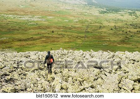 Stock Image - Caucasian hiker walking in rocky field. Fotosearch