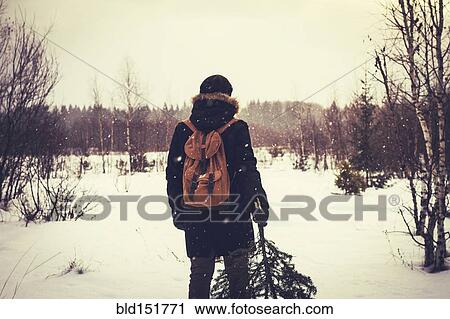 Stock Image - Caucasian man carrying tree in snowy field. Fotosearch