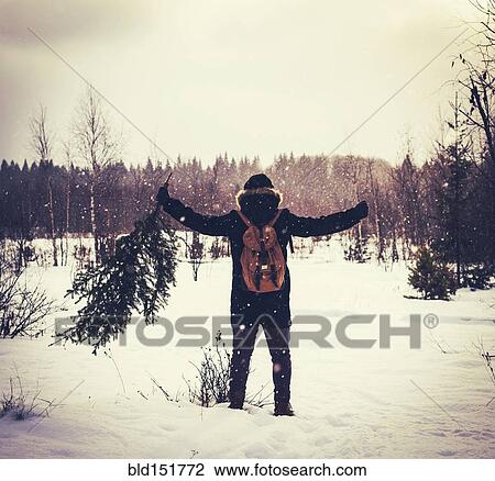 Stock Image - Caucasian man carrying tree in snowy field. Fotosearch