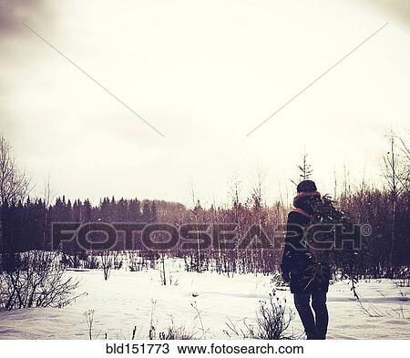 Stock Image - Caucasian man carrying tree in snowy field. Fotosearch