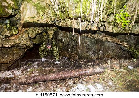 Stock Image - Caucasian man climbing out of rock formation cave. Fotosearch