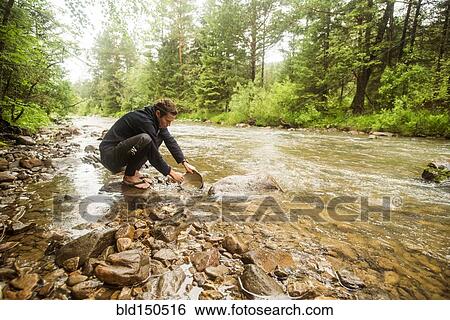 Stock Photograph - Caucasian man crouching in forest river. Fotosearch
