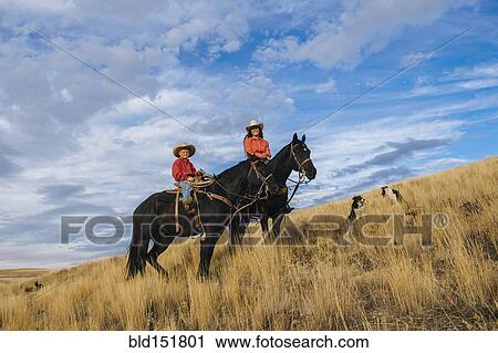 Stock Image - Caucasian mother and son on horseback on grassy hill. Fotosearch