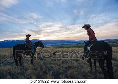 Stock Image - Caucasian mother and son riding horses in remote field. Fotosearch