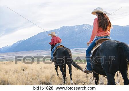 Stock Photo - Caucasian mother and son riding horses in grassy field. Fotosearch