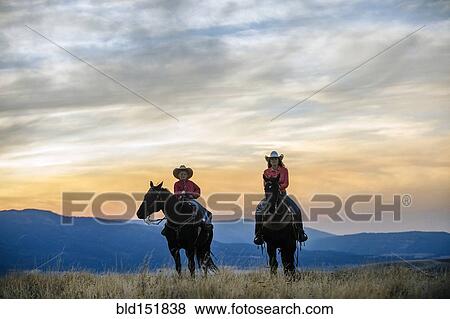 Stock Photo - Caucasian mother and son riding horses in grassy field. Fotosearch