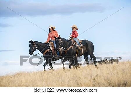 Stock Photograph - Caucasian mother and son riding horses in grassy field. Fotosearch