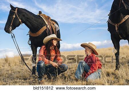 Stock Image - Caucasian mother and son with horses in grassy field. Fotosearch