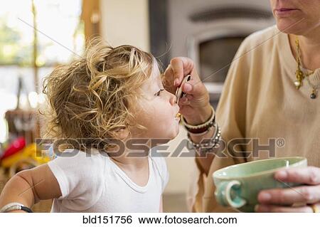Stock Photograph - Caucasian mother feeding baby son in high chair. Fotosearch