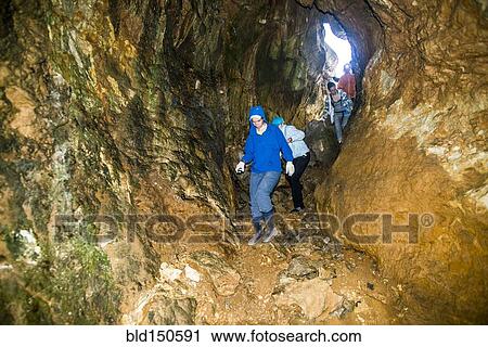 Stock Image - Caucasian people exploring rock formation cave. Fotosearch