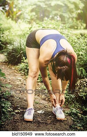 Stock Photo - Caucasian runner checking ankle on trail in park. Fotosearch