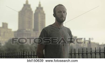 Stock Photo - Caucasian runner listening to earbuds in front of city skyline. Fotosearch