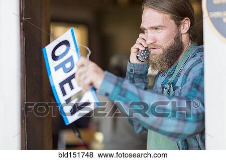 Stock Photo - Caucasian server on telephone hanging open sign on cafe window. Fotosearch