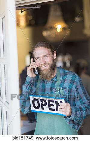 Stock Photo - Caucasian server on telephone hanging open sign on cafe window. Fotosearch