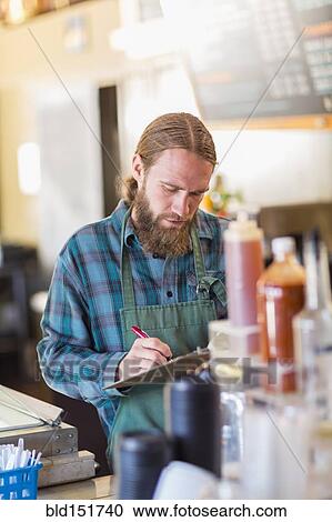 Stock Image - Caucasian server writing on clipboard in cafe. Fotosearch
