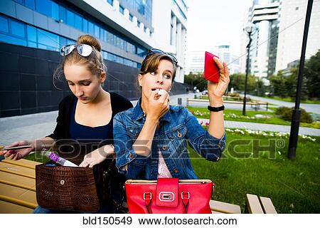Stock Photo - Caucasian woman applying makeup on park bench. Fotosearch