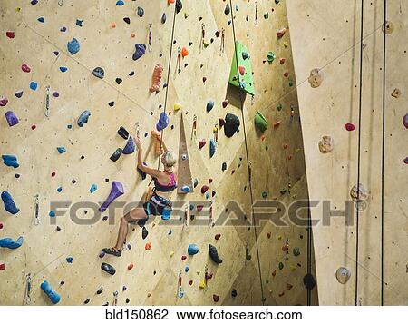 Stock Image - Caucasian woman climbing indoor rock wall. Fotosearch