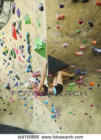 Stock Photograph - Caucasian woman climbing indoor rock wall. Fotosearch