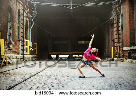 Stock Image - Caucasian woman dancing on cobblestone street. Fotosearch