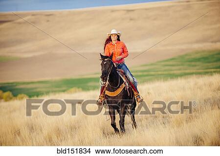 Picture - Caucasian woman riding horse in grassy field. Fotosearch
