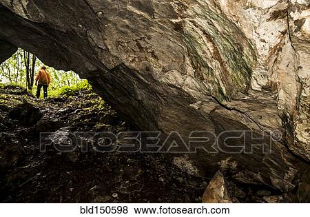 Stock Photo - Caucasian woman standing outside rock formation cave. Fotosearch