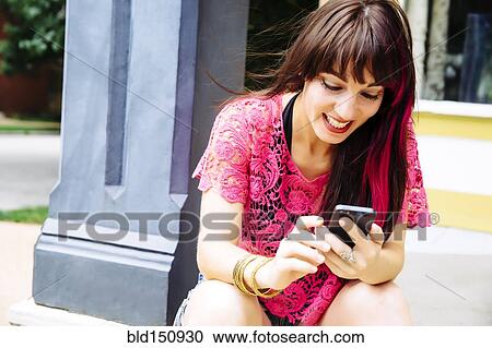 Stock Image - Caucasian woman using cell phone on sidewalk. Fotosearch
