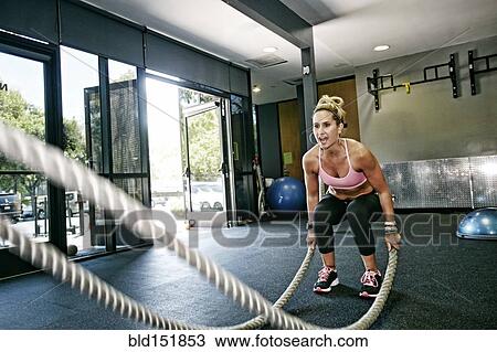 Stock Image - Caucasian woman working out with ropes in gym. Fotosearch