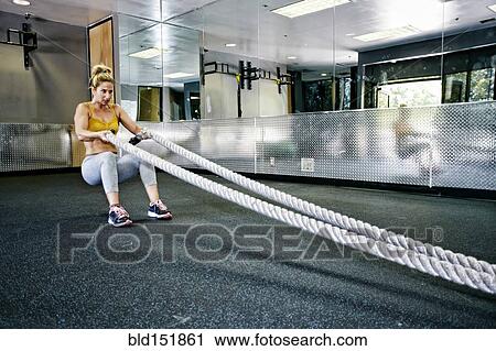 Stock Image - Caucasian woman working out with ropes in gym. Fotosearch