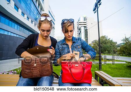 Stock Photo - Caucasian women searching in purses on park bench. Fotosearch