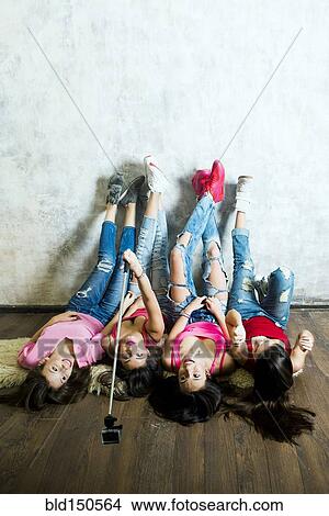 Picture - Caucasian women taking cell phone selfie on floor. Fotosearch