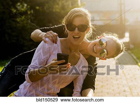 Stock Photo - Caucasian women taking cell phone selfie. Fotosearch