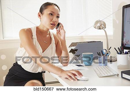 Stock Photo - Chinese businesswoman talking on cell phone at desk. Fotosearch