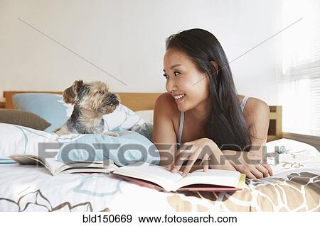 Stock Photo - Chinese woman relaxing with dog on bed. Fotosearch
